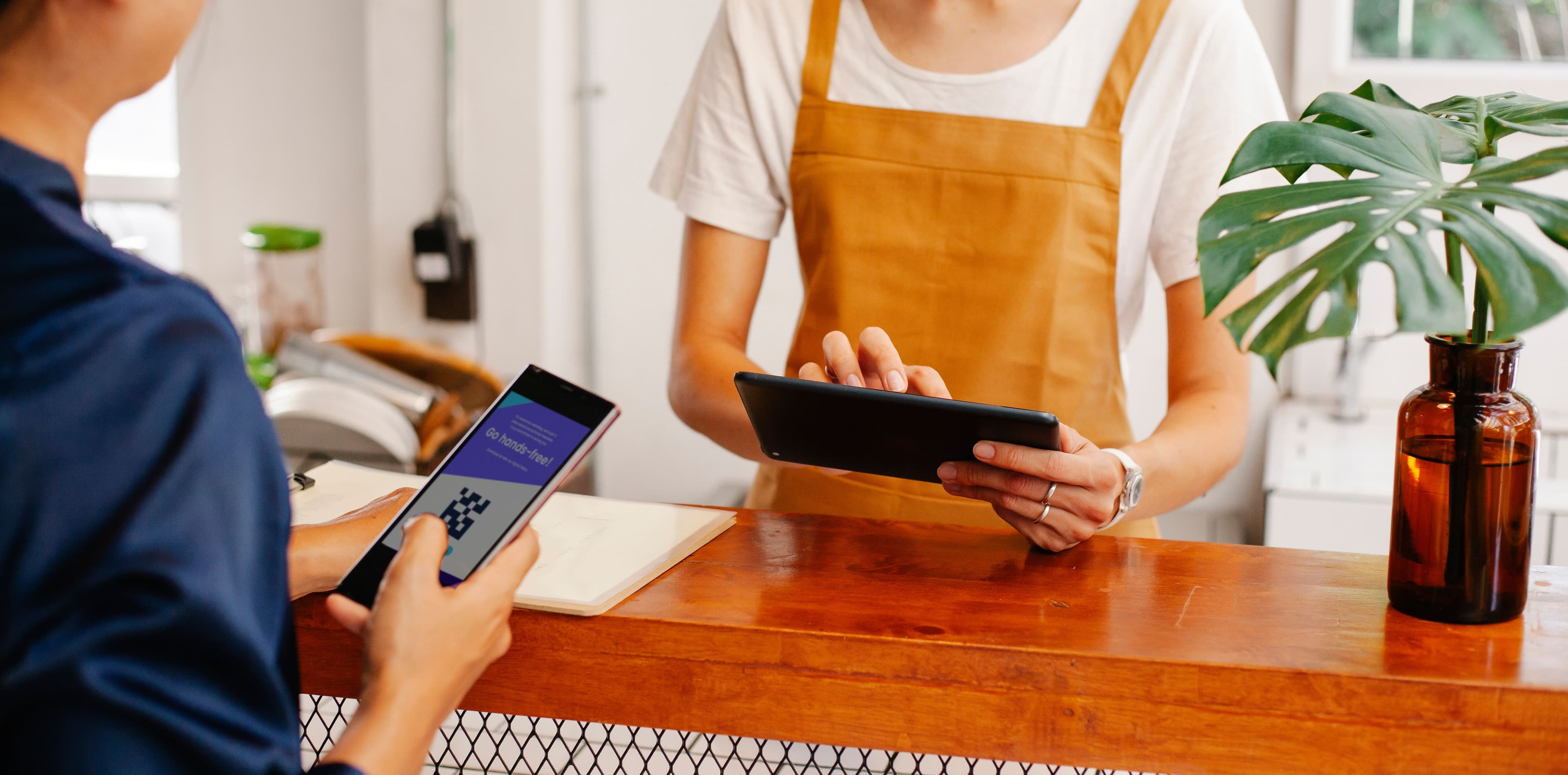 Client qui scanne un QR code au comptoir pendant qu'un membre du personnel utilise une tablette