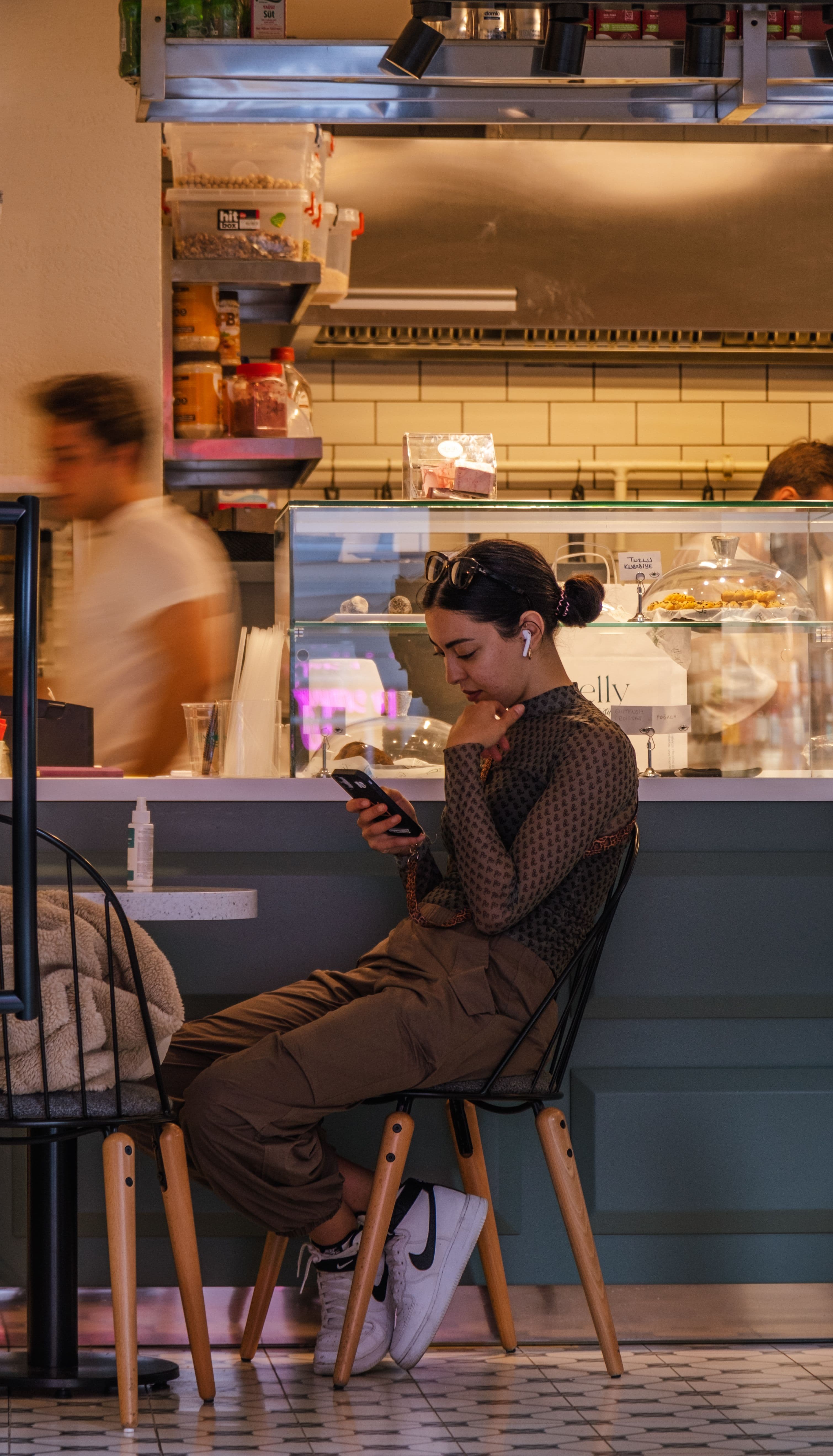 Cliente souriante qui consulte son téléphone accoudée au comptoir d'un café