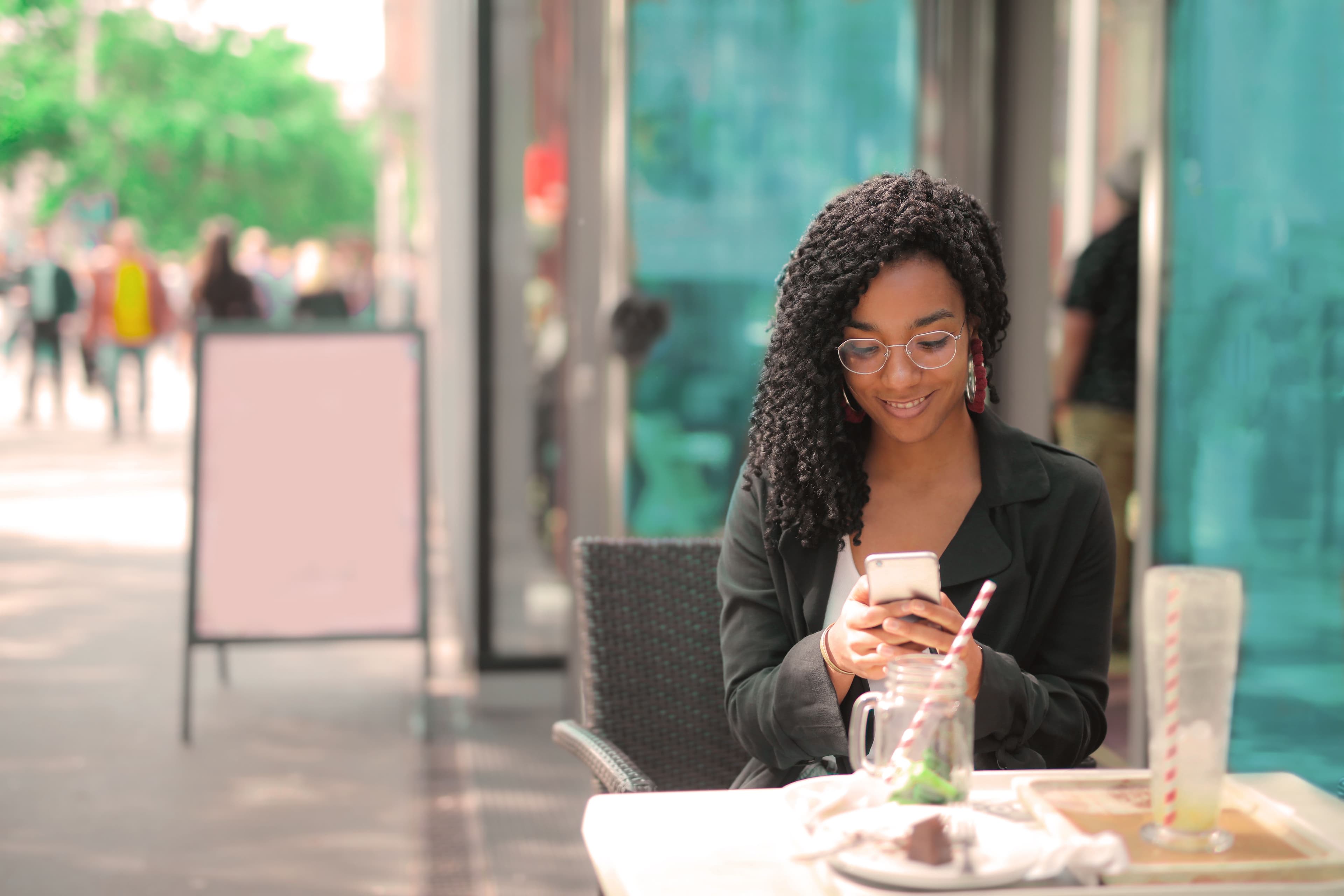 Cliente souriante consultant son téléphone en terrasse d'un café